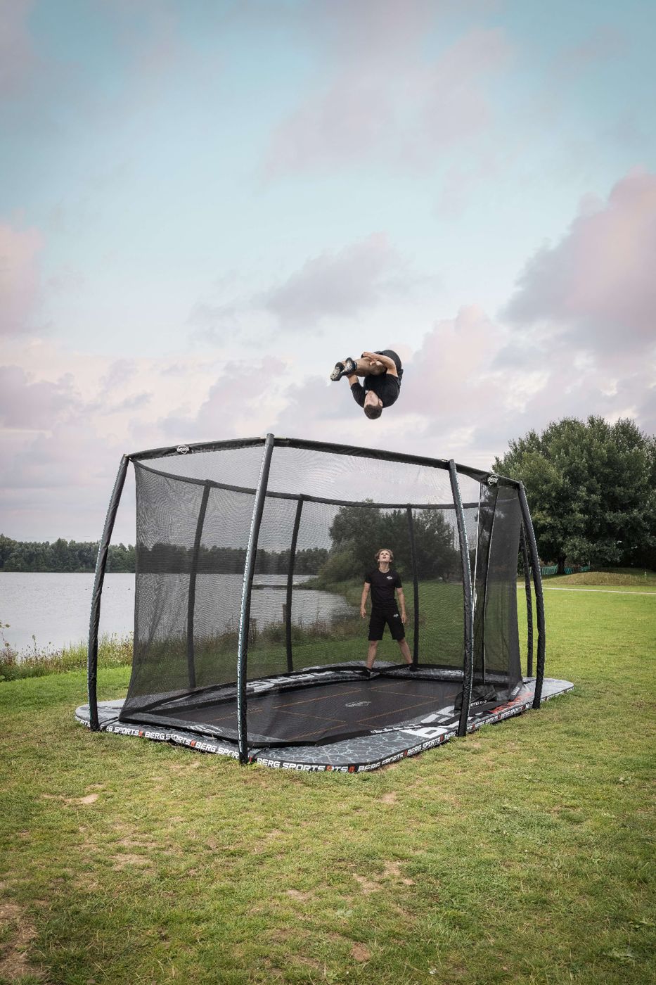 BERG Pro Bouncer FlatGround trampoline with a safety net, set level with the grass beside a lake