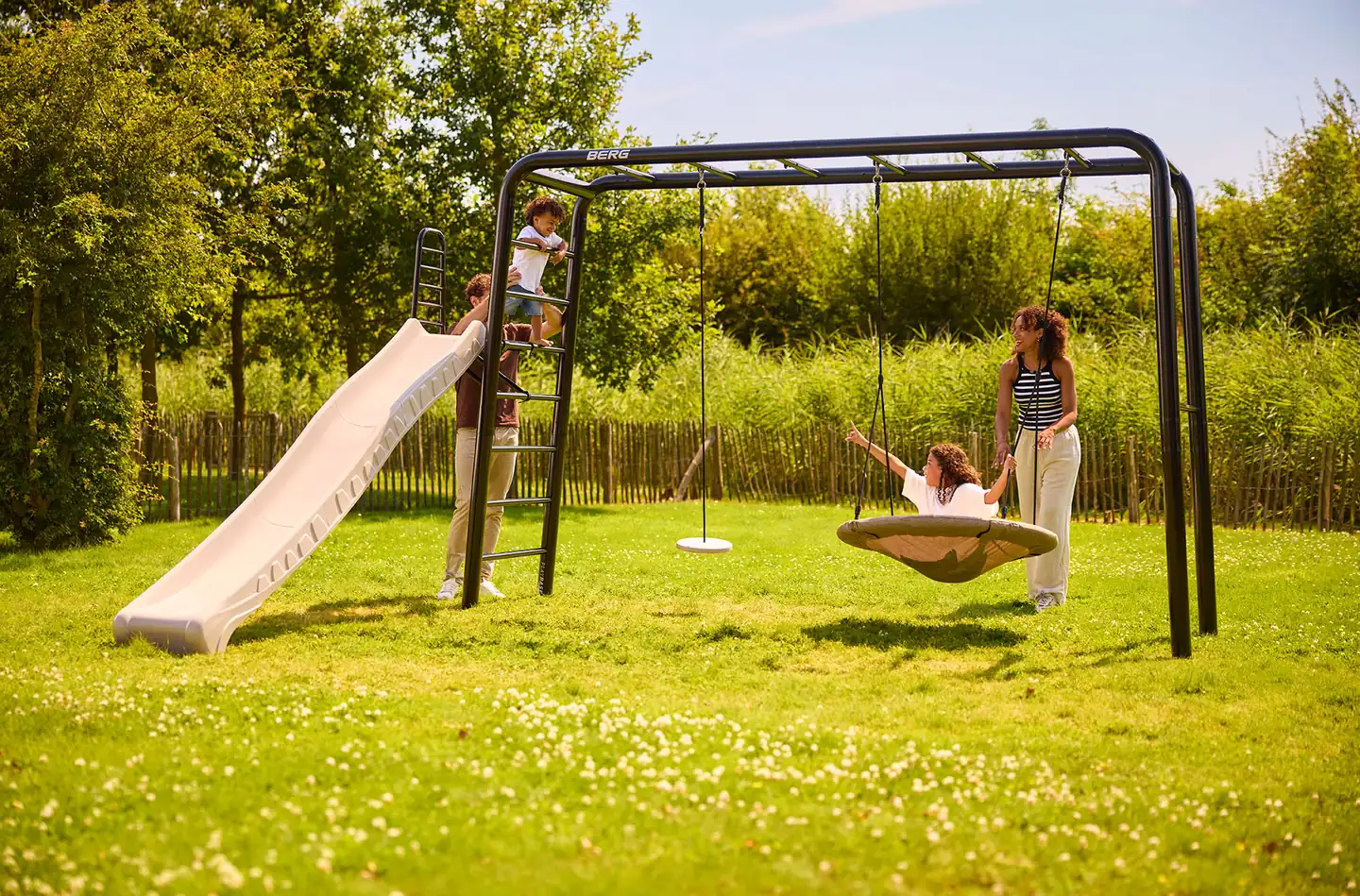 Children playing on a BERG PlayBase climbing frame fitted with a slide and a nest swing